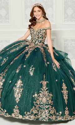 A woman in a jeweled tiara wears the Quinceanera Dress PR30112 By Princesa—an off-the-shoulder emerald gown with gold embroidery and a full tulle skirt—while standing in an ornate, light-colored room.