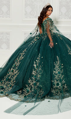 A woman wearing the Quinceanera Dress PR30114 By Princesa, featuring gold embroidery and a long train, stands before a white wall with a tiara, glancing over her shoulder.