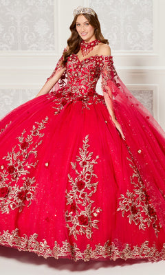 A woman stands indoors against a decorated white wall, wearing the Quinceanera Dress PR30114 By Princesa—an elaborate, bright red off-the-shoulder gown with gold floral embroidery and a matching crown.
