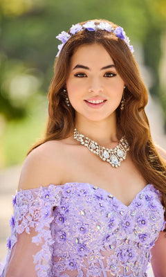 A young woman smiles outdoors in the Quinceanera Dress PR30116 By Princesa, a lavender off-shoulder lace gown, paired with a floral headband and a large jeweled necklace.