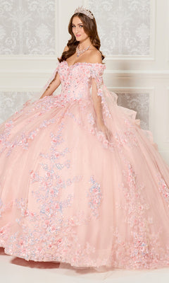 A woman in the Quinceanera Dress PR30116 By Princesa, featuring a pink off-the-shoulder design with floral details and a fitted corset bodice, wears a tiara as she stands before an ornate white wall.