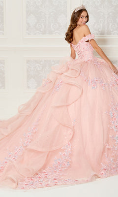 A young woman in a tiara wears the Quinceanera Dress PR30116 By Princesa, featuring an off-the-shoulder design with floral embellishments, corset bodice, and a long layered train, standing in an elegant room.