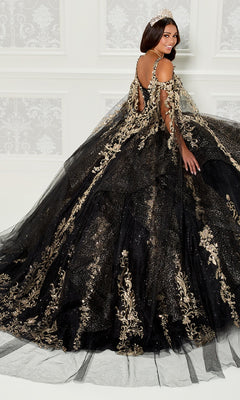 A woman in the Quinceanera Dress PR30117 By Princesa, featuring black fabric with gold embroidery and glitter, stands before a white patterned wall, smiling as she looks over her shoulder.