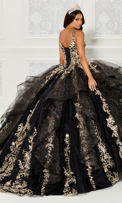 A woman wearing a tiara and the Quinceanera Dress PR30117 By Princesa, featuring ornate black fabric with gold embroidery and glitter, stands in front of a white decorative wall.