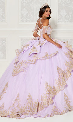 A woman wearing the Quinceanera Dress PR30118 By Princesa with a tiara stands before an ornate white wall, looking over her shoulder and smiling.