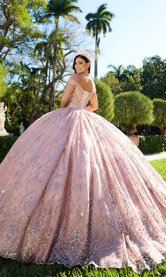 A young woman poses outdoors among palm trees wearing the Princesa PR30132 beaded quinceanera dress, a light pink off-the-shoulder gown adorned with sparkling embellishments.