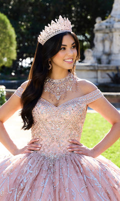 A woman wearing the Princesa PR30132 Beaded Quinceanera Dress and an ornate crown stands outdoors, smiling with her hands on her waist.