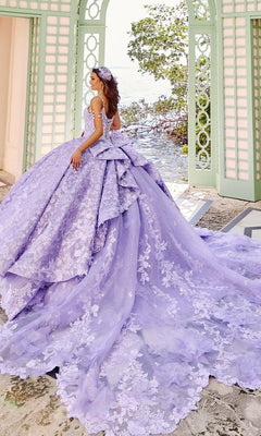 Wearing the Quinceanera Dress PR30139 by Princesa, a woman in a glitter tulle ball gown with lace details and a long train stands at open mint-green doors, looking back toward lush greenery outside.