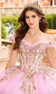 A young woman wearing a gold crown and ornate jewelry poses outdoors in the Quinceanera Dress PR30152 By Princesa, featuring ombre fabric with gold embroidery, looking at the camera.