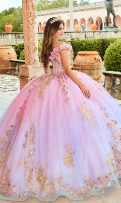 A young woman in the Quinceanera Dress PR30152 By Princesa, adorned with shimmering sequins and gold accents, stands on a terrace with classical architecture, large urns, and a delicate tiara.
