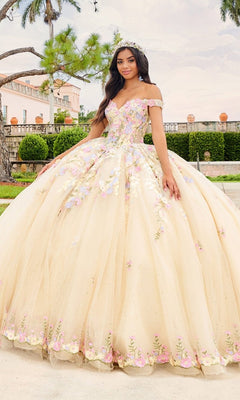 A woman stands outdoors near a grand building and lush gardens, wearing the Quinceanera Dress PR30155 By Princesa—an off-shoulder pastel yellow ball gown with 3D floral embroidery and a cathedral train.