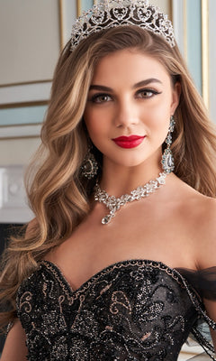 Woman in Quinceanera Dress PR30160 By Princesa—an ornate black off-the-shoulder gown—pairs jeweled tiara, matching necklace, and earrings while posing in an elegant, upscale interior.