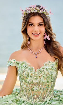 A young woman smiles and poses outdoors in the PR30162 Quinceanera Dress by Princesa—a sparkly, floral green off-the-shoulder gown with a glitter tulle skirt and a flower crown.