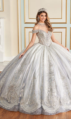 A woman in the Quinceanera Dress PR30173 By Princesa, paired with a tiara and necklace, stands indoors before a decorated wall.