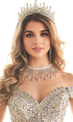 A woman poses against a white background wearing the Quinceanera Dress PR30173 By Princesa, paired with a jeweled crown, elaborate earrings, and a matching sparkling necklace.