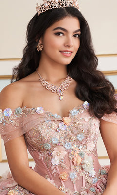 A young woman with long dark hair wears the Princesa Quinceanera Dress PR30175, paired with a jeweled tiara, necklace, and earrings, as she poses indoors and smiles.