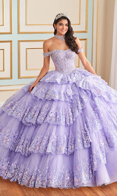A young woman stands indoors against a decorated wall, wearing the Princesa Quinceanera Dress PR30181 in lavender with layered ruffles, floral embellishments, and a tiara.