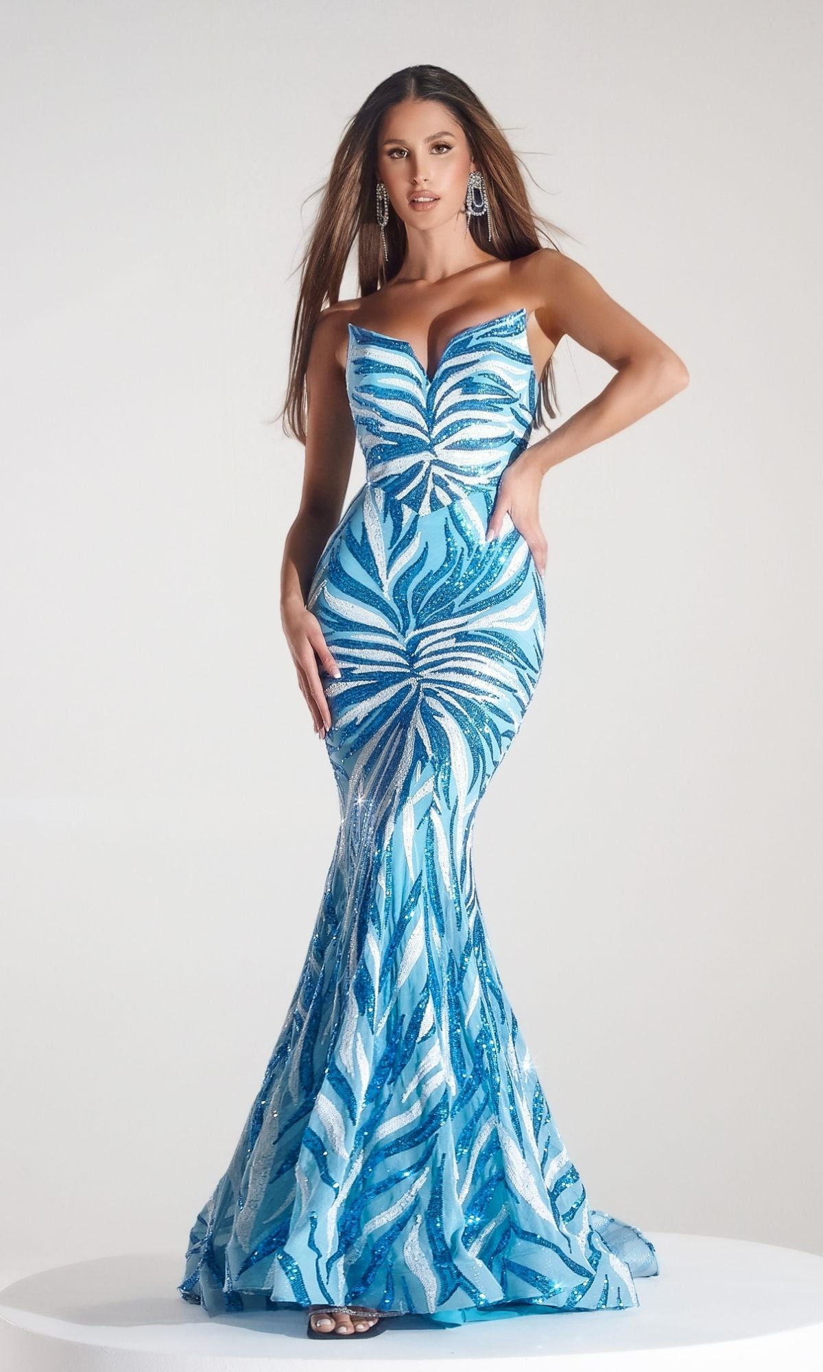 A woman poses with one hand on her hip in the Long Prom Dress PS22538 by Portia and Scarlett—a fitted, floor-length blue and white mermaid gown with a strapless sweetheart bodice—against a plain light background.