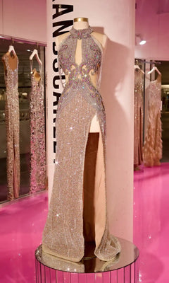 The Long Prom Dress PS23704C by Portia and Scarlett, a sparkling pink off-the-shoulder beaded gown with a high slit and sheer illusion details, is displayed on a mannequin in front of mirrors and similar dresses on a pink floor.