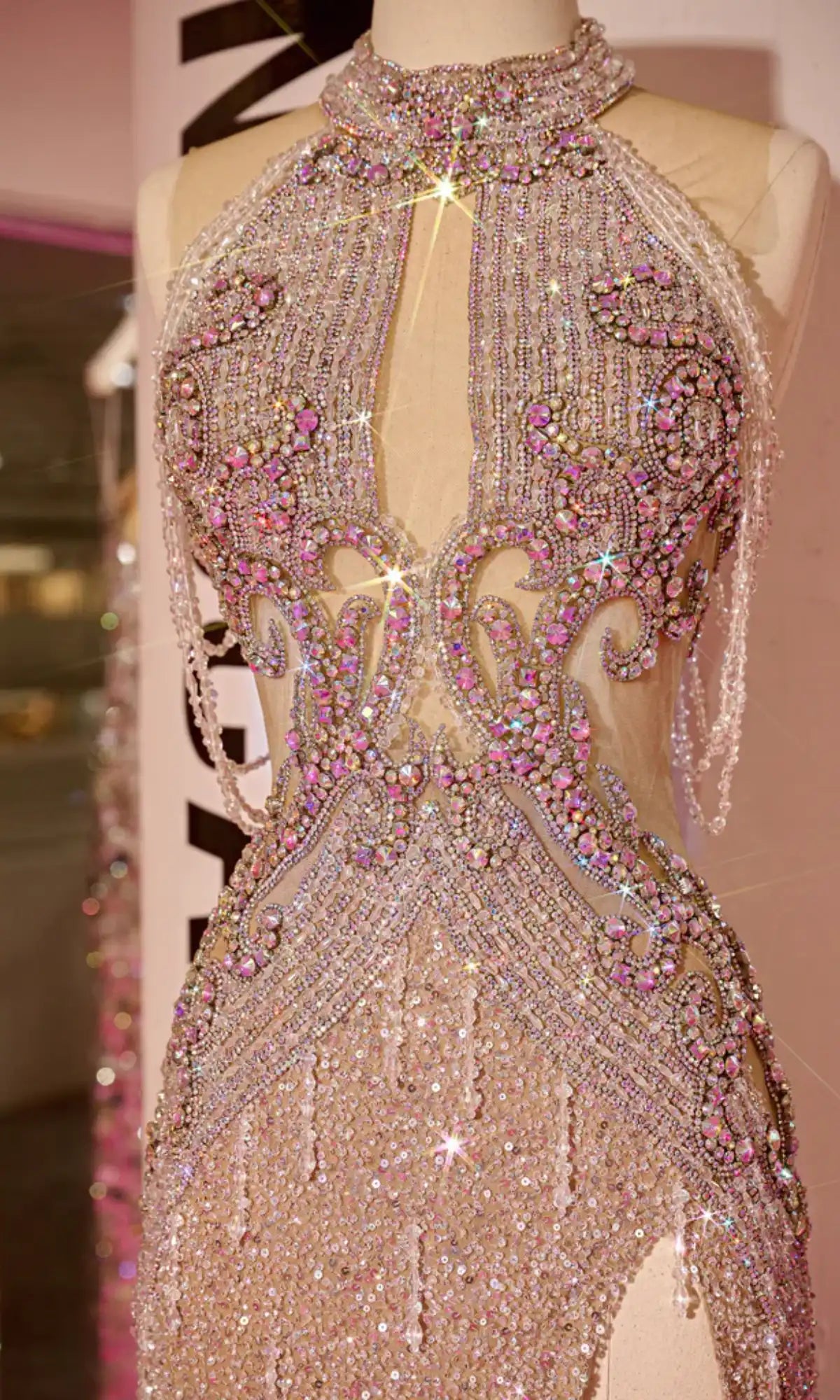 A mannequin showcases the Long Prom Dress PS23704C by Portia and Scarlett, featuring sparkling beading, a high neckline, cut-out accents, sheer illusion details, and ornate pink and silver patterns.