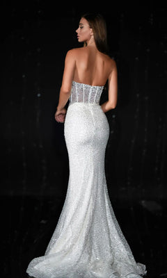 A woman stands elegantly against a dark background, wearing the Long Prom Dress PS24942 by Portia and Scarlett—a form-fitting white strapless corset gown with a sheer beaded bodice and a long sequined train.