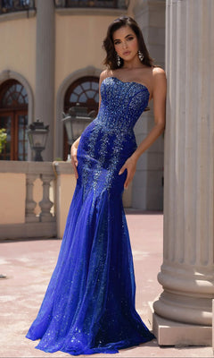 A woman stands outdoors by a grand column in the Portia and Scarlett PS25169, a fitted, strapless lace mermaid prom dress with sparkling embellishments.