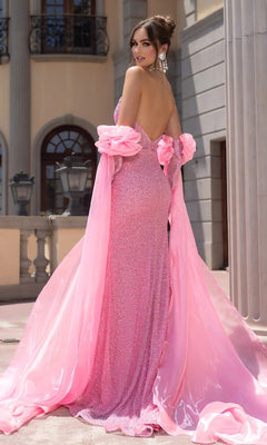 A woman in the Portia and Scarlett PS25176 long prom dress, featuring a sparkling strapless sequin design and flowing train, stands outside a classical building, glancing over her shoulder.