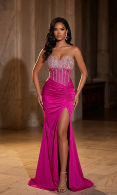 Woman in the Portia and Scarlett PS25181 long prom dress in hot pink, featuring a strapless sweetheart neckline, crystal-embellished corset, beaded bodice, and high leg slit, standing in a marble hall.