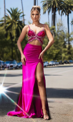 A woman poses outdoors in the Portia and Scarlett PS25264 long prom dress in hot pink, featuring rhinestone embellishments, a high slit, and spaghetti straps; palm trees and parked cars are seen behind her.