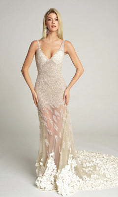 A woman stands against a plain background wearing the Portia and Scarlett PS25987C long formal dress in white, featuring a fitted bodice, illusion skirt, sequin detailing, and floral appliqué at the hem.