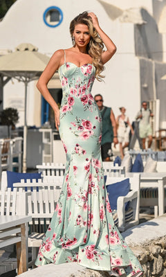 A woman in the Portia and Scarlett PS26000 long prom dress with a fitted floral mermaid silhouette stands outdoors in a sunny, whitewashed Mediterranean setting.