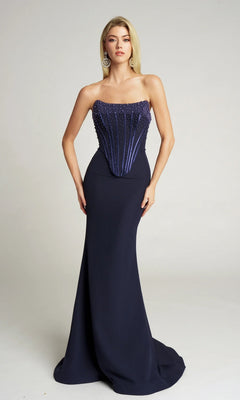 A woman wears the Portia and Scarlett PS26008 long formal dress in navy, featuring a strapless beaded corset bodice and floor-length skirt, against a plain light background.
