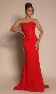 A woman poses against a beige background in the Portia and Scarlett PS26008 long formal dress, a red strapless evening gown with a beaded corset, floor-length skirt, and intricate detailing.