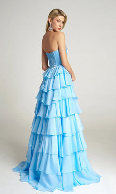 A woman wears the Portia and Scarlett PS26024 Long Prom Dress—a strapless, light blue gown with a tiered ruffle skirt and velvet corset bodice—standing slightly turned away from the camera against a plain background.
