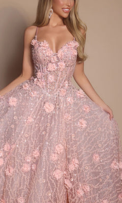 A woman in the Portia and Scarlett PS26027 long formal dress—a light pink, a-line gown with floral embellishments and thin straps—holds out the flowy skirt against a beige background.