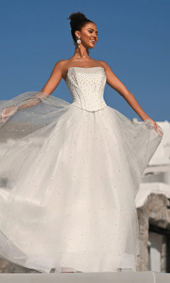 A woman stands outdoors under a clear blue sky, holding out the glitter tulle skirt of the white Portia and Scarlett PS26034 long formal dress with bead embellishments and a structured corset bodice.