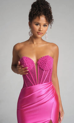 A woman poses against a neutral background wearing the Portia and Scarlett PS26039 long prom dress, featuring a strapless beaded corset bodice and bright pink satin skirt.