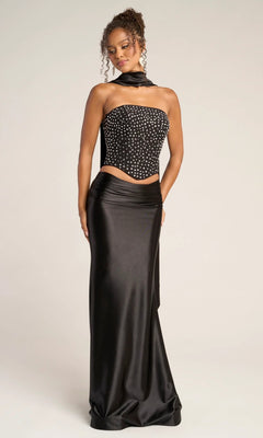 A woman stands against a plain background wearing the Portia and Scarlett PS26042, a long formal dress featuring a strapless black beaded corset top with choker-style scarf and fitted satin skirt.