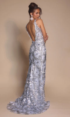 A woman poses in the Portia and Scarlett PS26043, a backless, floor-length formal dress with a sparkling finish and train, set against a beige backdrop.