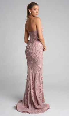 Woman wearing the Portia and Scarlett PS26074, a floor-length dusty pink gown with a strapless sweetheart neckline and floral lace appliqué, stands against a plain background looking over her shoulder.