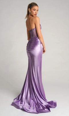 A woman in the Portia and Scarlett PS26085, a strapless lavender formal gown with an embellished corset bodice, sheer back panel, satin skirt, and ruched details, stands against a plain background.