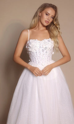 A woman poses elegantly in the Portia and Scarlett PS26146 Glitter Prom Ball Gown, featuring white glitter tulle, a boned-corset bodice with thin straps, and a full skirt against a neutral background.