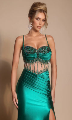 A woman models the Portia and Scarlett PS26158 long formal dress, featuring emerald green satin, a beaded corset bodice, sheer midsection, and high leg slit against a plain beige background.