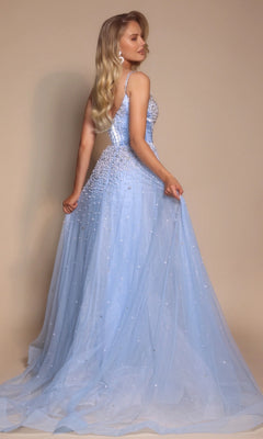 A woman with long blonde hair poses against a beige background wearing the Corseted Ball Gown: Portia and Scarlett PS26208, a light blue, floor-length gown with a sparkly boned-corset bodice, thin straps, and pearl embellishments.