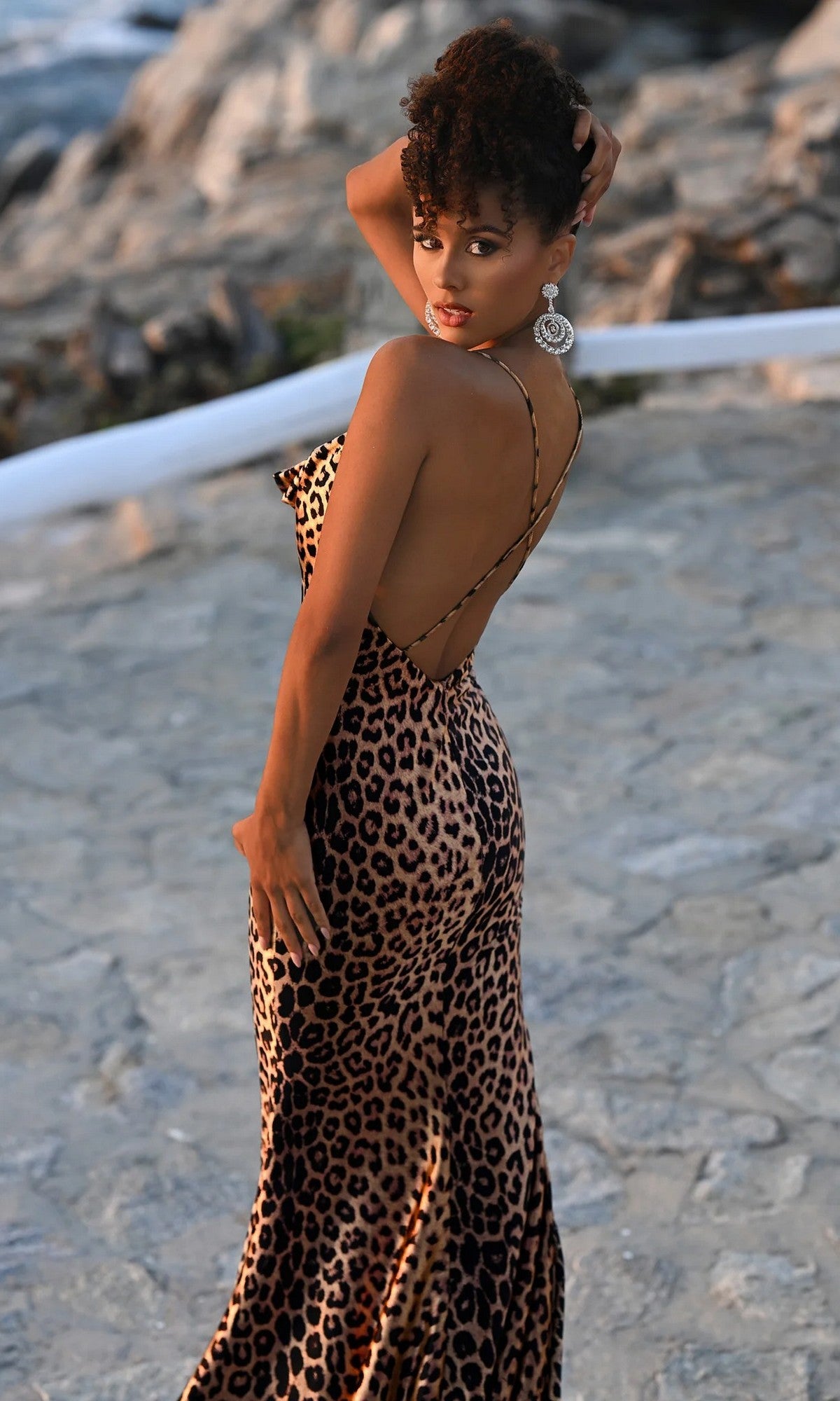 A woman poses outdoors on a stone pathway, looking over her shoulder at the camera while wearing the Portia and Scarlett PS26257 long prom dress.