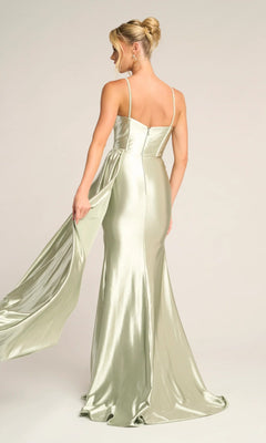 A woman in the Portia and Scarlett PS26270 long light green satin prom dress with thin straps stands facing away, holding part of the flowing fabric to the side.