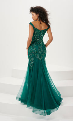 A woman stands on white steps, elegantly viewed from the back in the Long Prom Dress 14185 by Panoply—an off-the-shoulder, floor-length green mermaid gown with lace and sequin embroidered detailing.