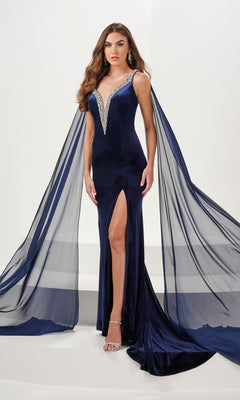 A woman stands against a white background wearing the Long Prom Dress 14198 by Panoply, a navy blue stretch velvet gown featuring a deep V-neckline, jeweled straps, sheer cape sleeves, high slit, and open back.