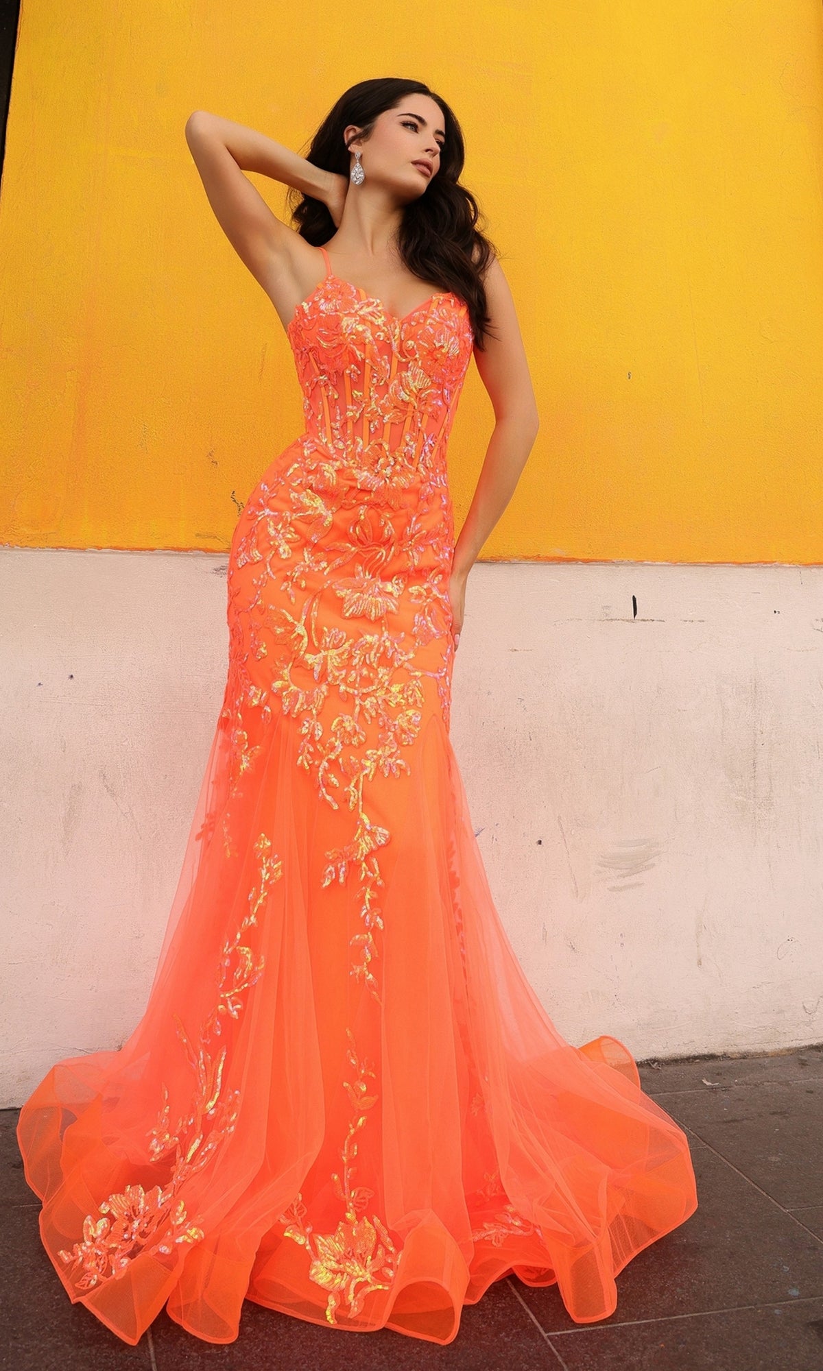 A woman poses by a yellow and white wall, wearing the Sequin-Lace Long Neon Mermaid Prom Dress Q1390—an eye-catching orange strapless gown featuring sequin-lace floral designs and sheer accents.