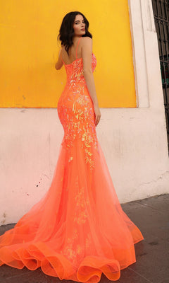 A woman in the Sequin-Lace Long Neon Mermaid Prom Dress Q1390, a bright orange form-fitting gown with floral designs, stands before a yellow and white wall, glancing over her shoulder.